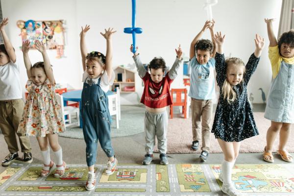 Children standing together with their arms raised during a play activity.