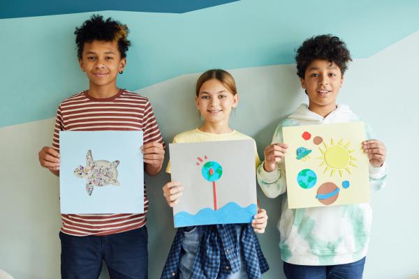 Three children holding up colourful paintings they have made.