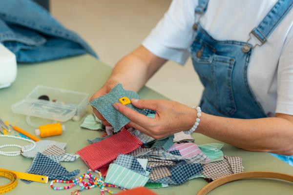 Hands making a fabric badge among colourful sewing materials.
