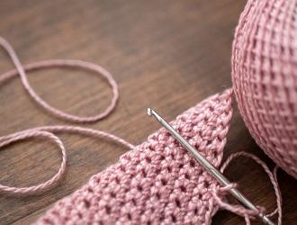 Pink yarn, a crochet hook and a partly crocheted piece on a table.