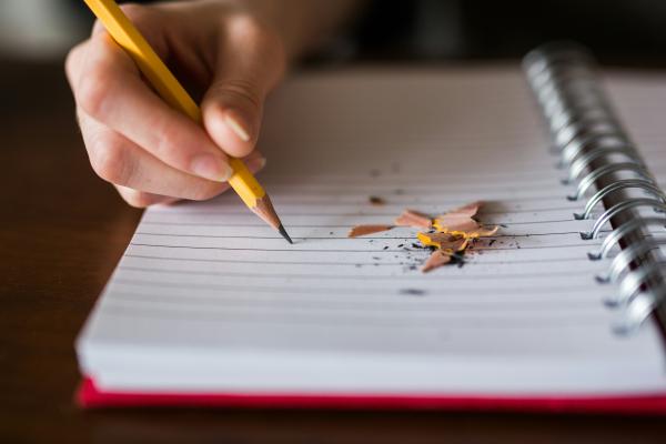 A hand writing with a pencil in a spiral notebook