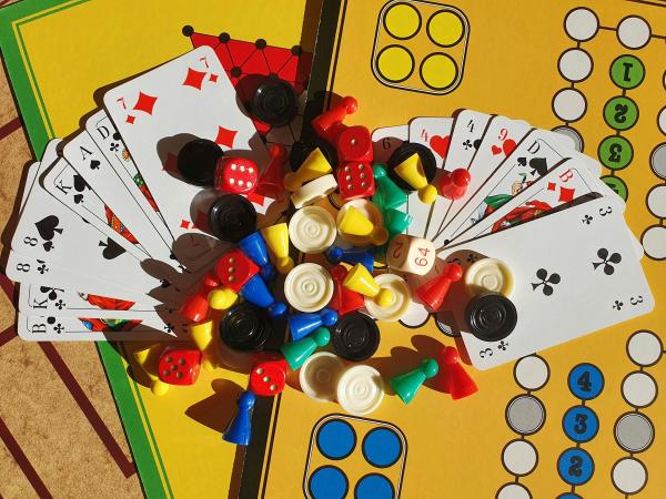 Playing cards, dice and colourful game pieces arranged on a board game.
