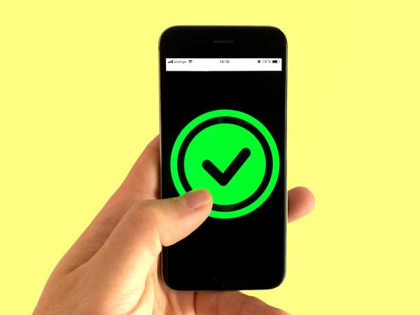 A hand holding a phone displaying a green verification check mark.