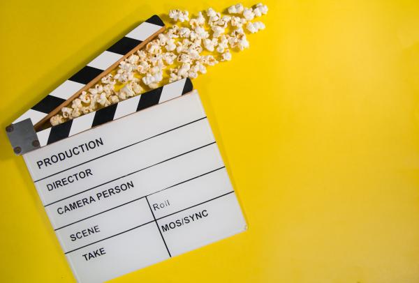 A film clapperboard and spilled popcorn on a bright yellow background.