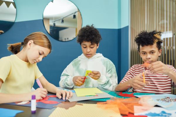 Three children making colourful paper crafts at a table.