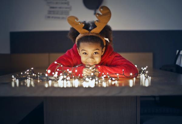 Child wearing a festive reindeer headband beside fairy lights, featured for the library festive story time.
