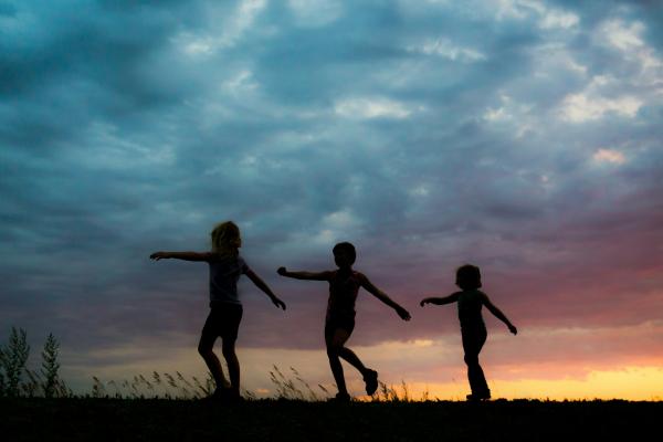 Three children silhouetted against a colourful evening sky.